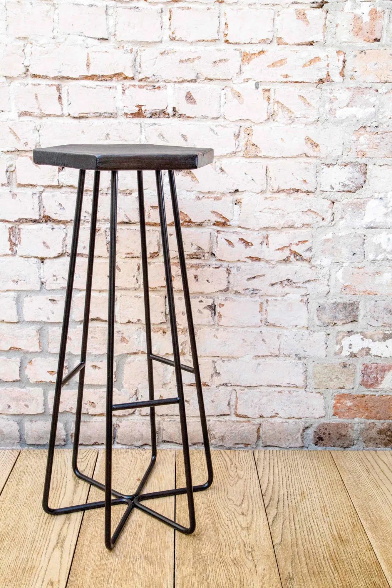 Éxi stool: dark hexagonal seat against brick wall.